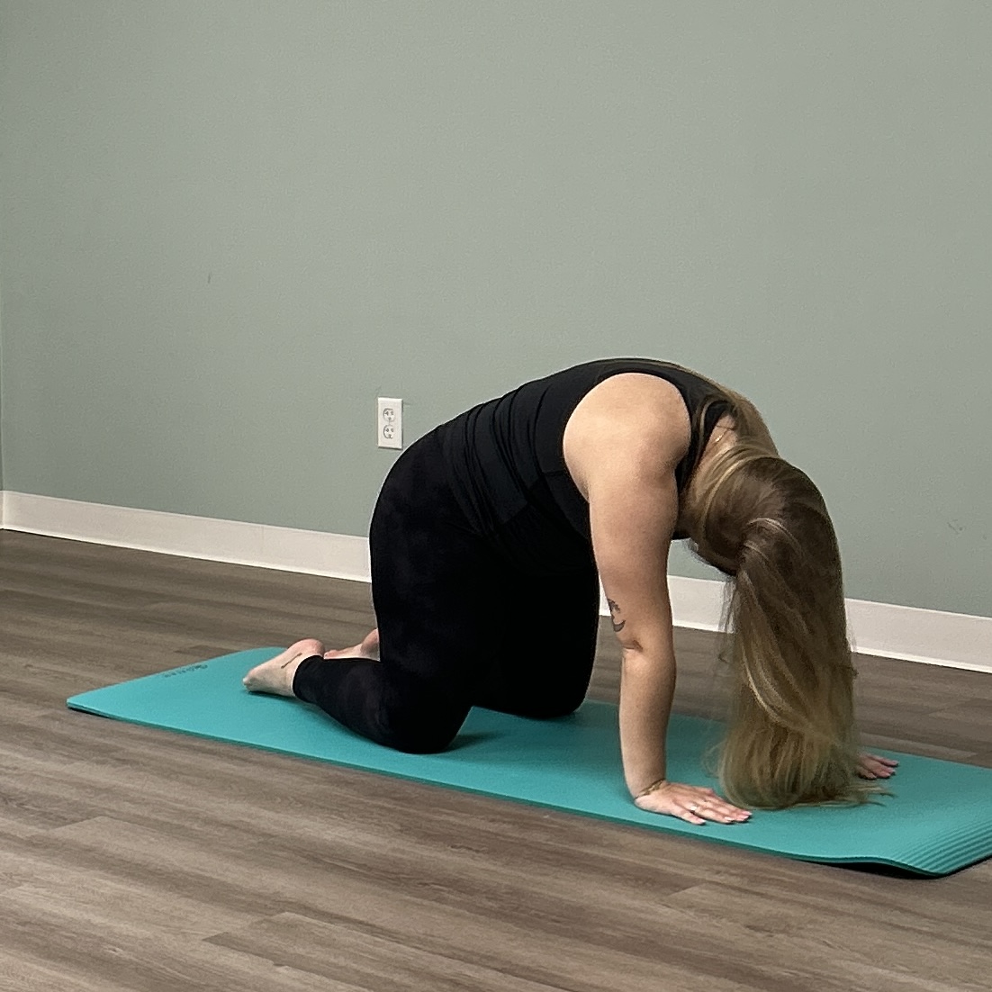Pregnant mama in child's pose on a teal yoga mat